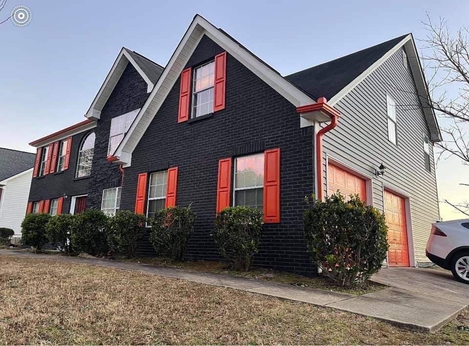 Black painted brick home with bright orange shutters and garage doors