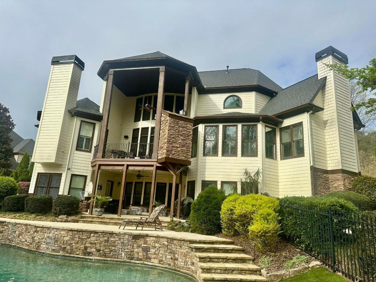 Rear of a cream-sided home with a stone and timber covered porch above a pool