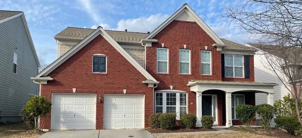 Red brick two-story with fresh white trim and garage doors